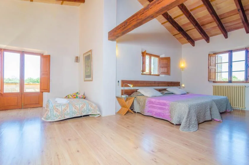 A bedroom with a bed, exposed wooden ceiling beams, and several windows.