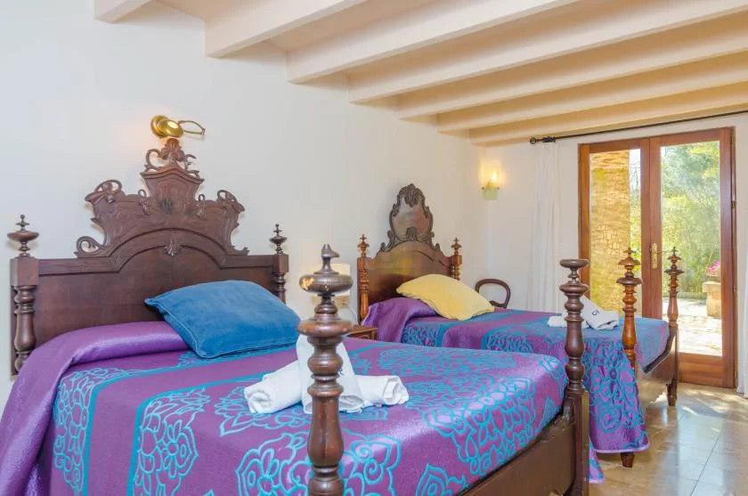 A bedroom with two beds dressed in colorful patterned bedding beside glass doors.