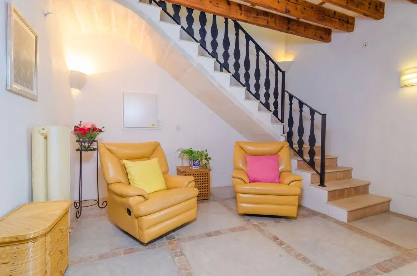 A bright sitting area has two armchairs beneath a staircase.