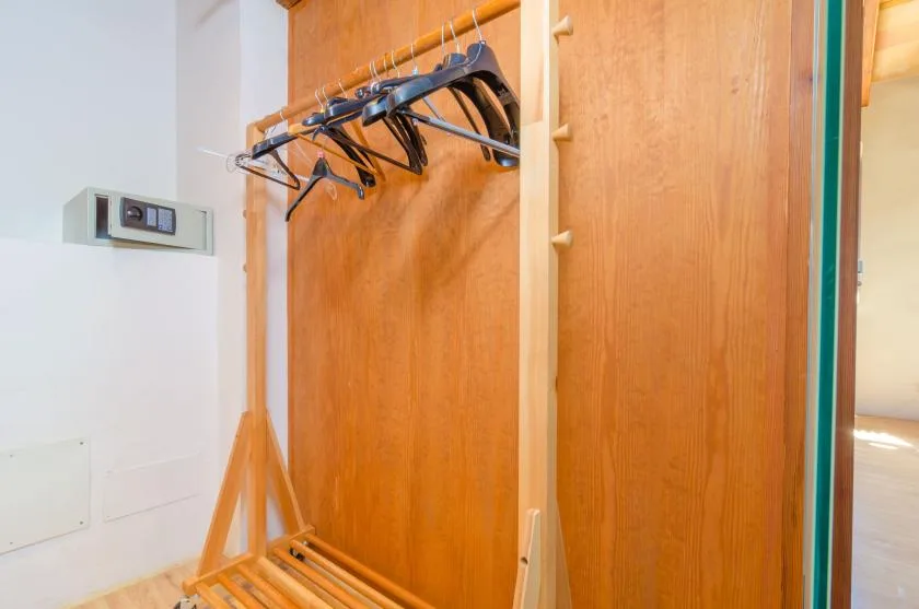 An open wooden wardrobe with hangers and a luggage rack.