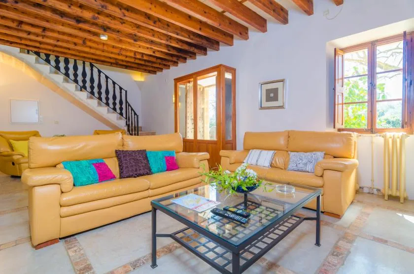 A bright living room with tan seating, a glass coffee table, and a wooden-beam ceiling.