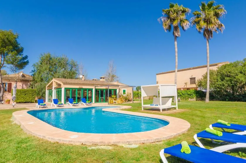 A swimming pool sits beside a grassy lawn and several lounge chairs.