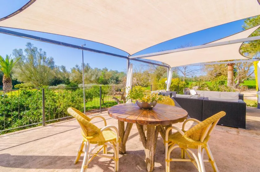 An outdoor dining area with a round wooden table and woven chairs under a canopy.