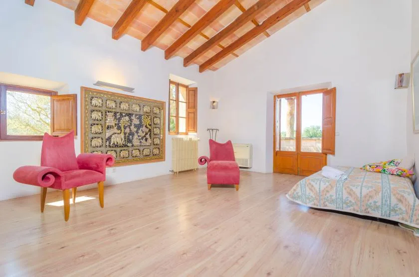 A bright bedroom with exposed wooden ceiling beams and colorful seating.