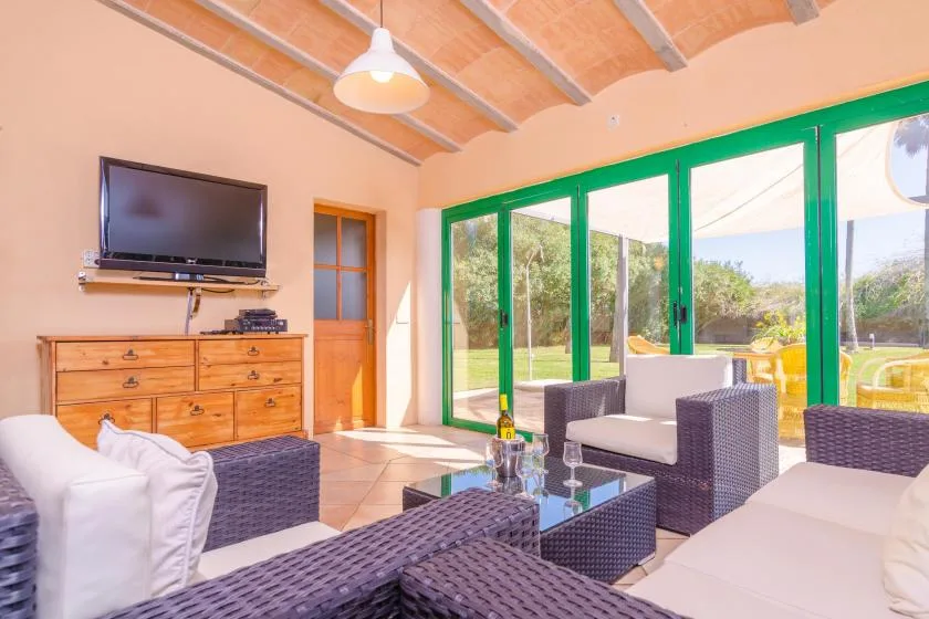 A bright living room with wicker seating and green-framed glass doors opening to a garden.
