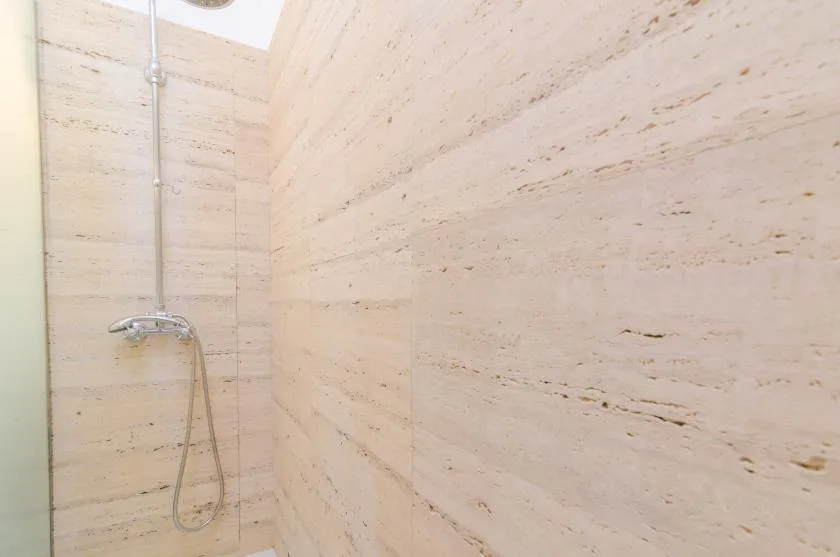 A tiled shower area with a wall-mounted showerhead and handheld hose.