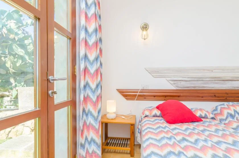 A bedroom with a bed covered in colorful zigzag-patterned bedding beside a glass door.