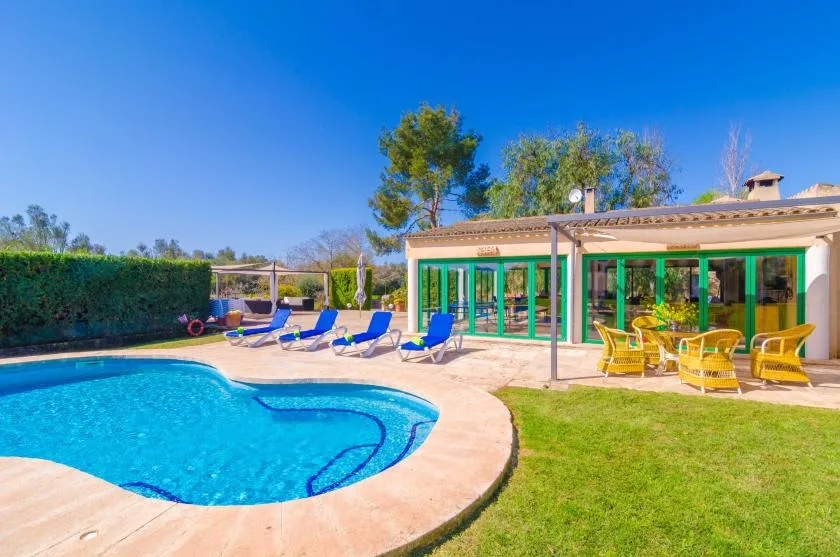 A swimming pool beside a patio with seating and a glass-fronted building.