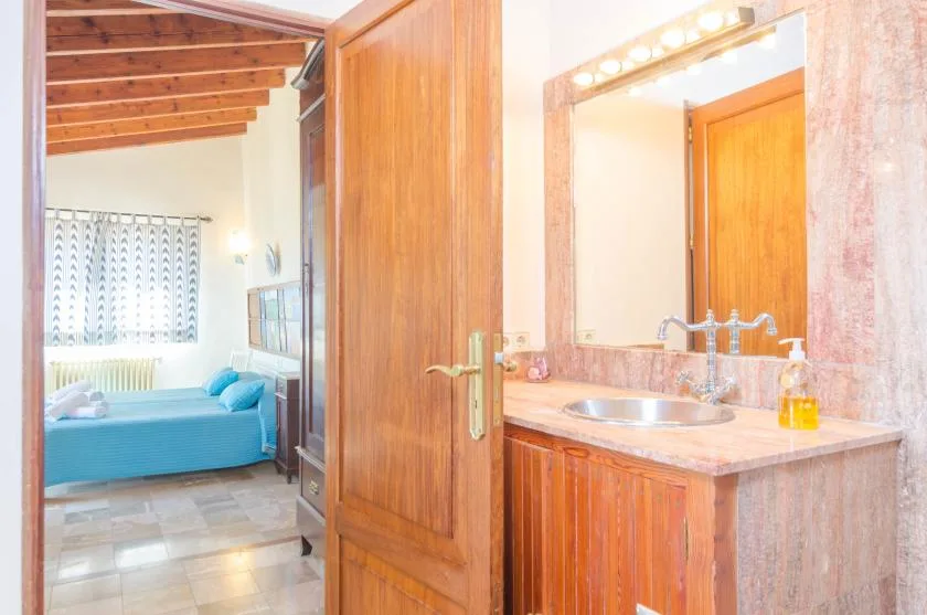 A bathroom vanity with a sink and mirror opens onto a bedroom with blue bedding.