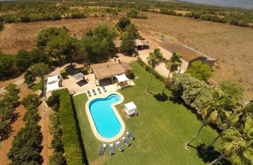 An aerial view of a swimming pool and landscaped grounds surrounded by dry fields.
