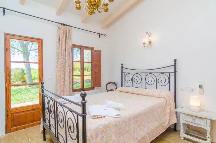 A bedroom with a metal bed frame and windows overlooking greenery.
