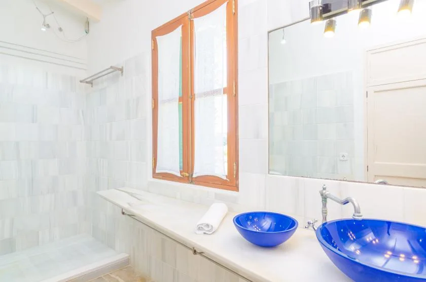 A bright bathroom with a long vanity, two blue vessel sinks, and an orange-framed window.