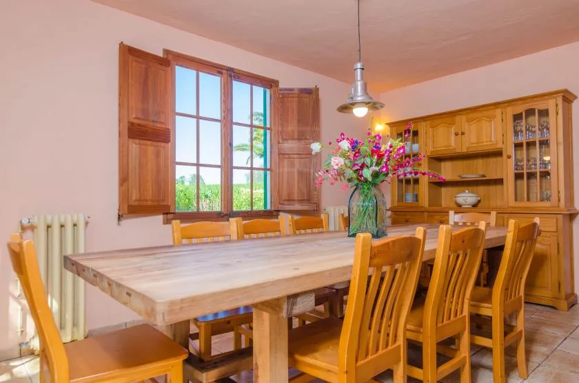 A wooden dining table and chairs sit beside a large window in a dining room.