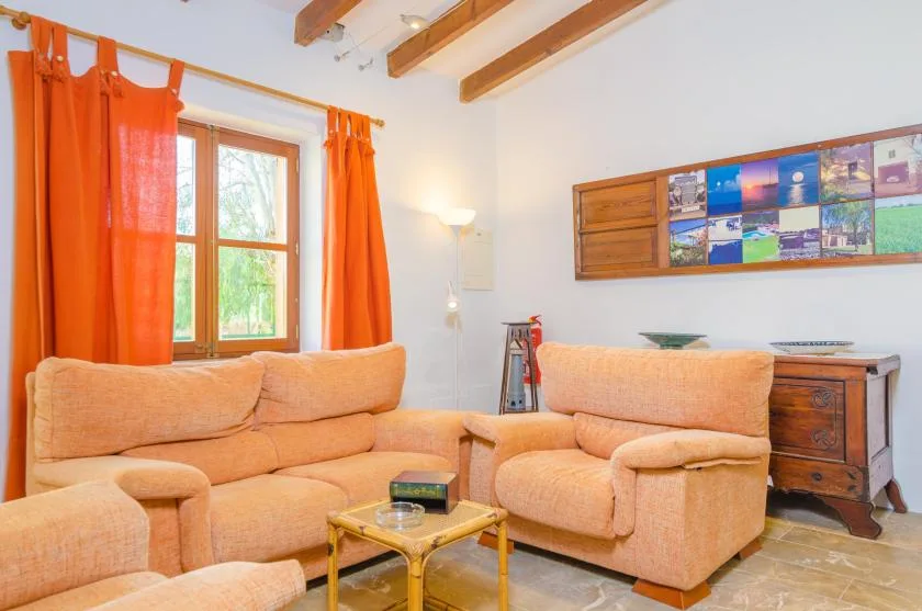 A living room with orange seating, bright curtains, and exposed ceiling beams.
