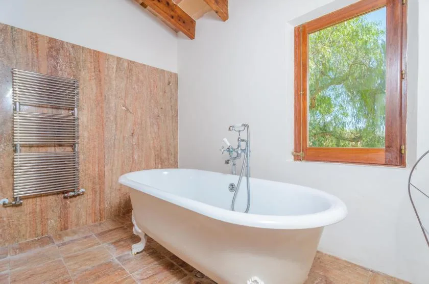 A bathroom with a freestanding bathtub beneath a wood-framed window.