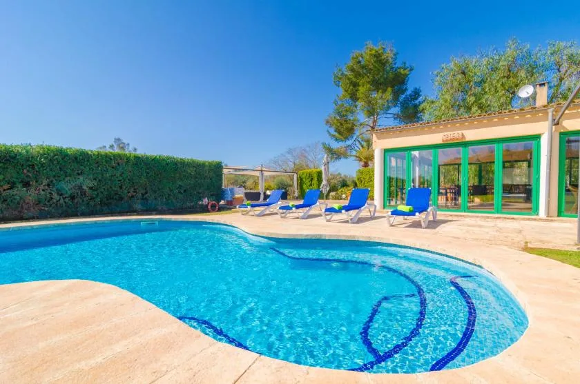 An outdoor swimming pool beside a patio with lounge seating and a glass-fronted building.