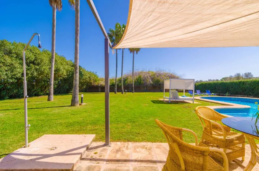 A grassy outdoor pool area with seating beneath a shade canopy.