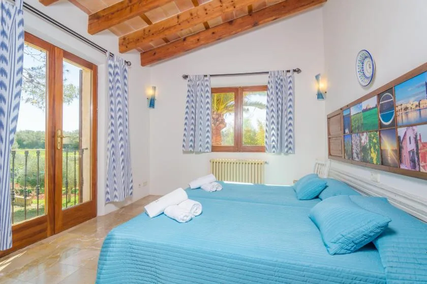 A bedroom with a large bed, wooden beams, and windows opening onto a balcony.