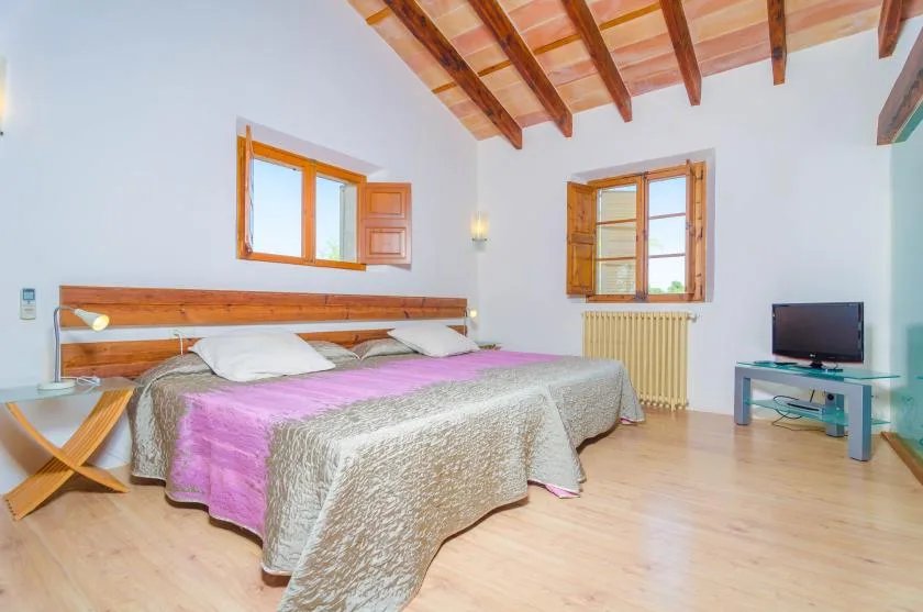 A bedroom with two beds, wooden ceiling beams, and windows.