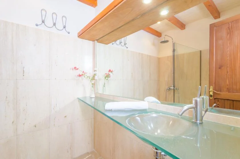A tiled bathroom with a glass vanity and a shower in the background.