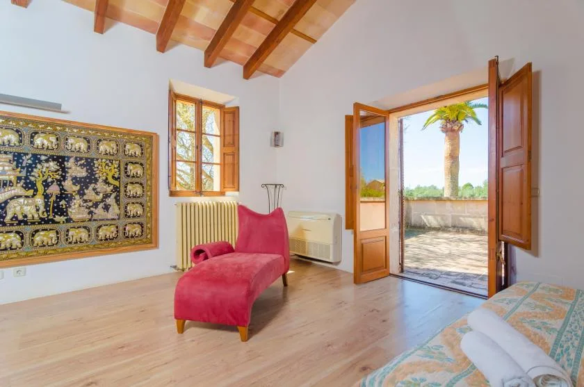 A bright bedroom with a red chaise lounge and open doors leading to a terrace.