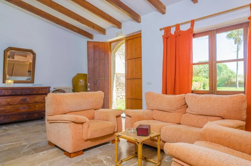 A living room with peach-colored seating, wooden ceiling beams, and an open doorway.