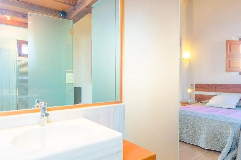 A bedroom with a bed beside a bathroom vanity and glass shower.