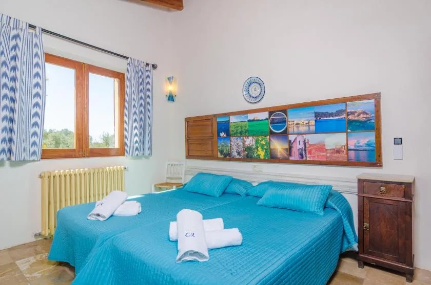 A bedroom with a turquoise bed, folded towels, and a window with patterned curtains.
