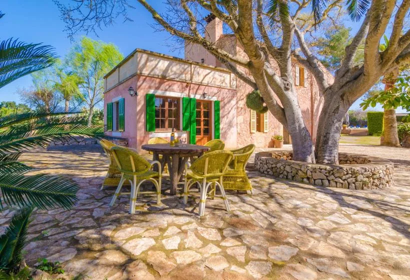 A stone-paved outdoor patio beside a pink building, with a table and seating under a large tree.