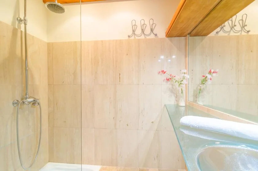 A tiled bathroom with a glass shower, a basin, and a folded towel.