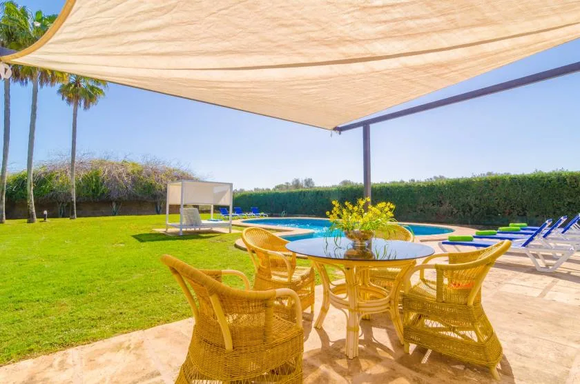 Una zona de comedor exterior da a una piscina y un césped bajo una cubierta de sombra.