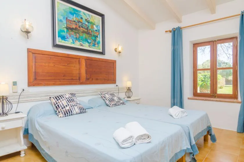 A bedroom with a large bed, blue bedding, and a window overlooking greenery.