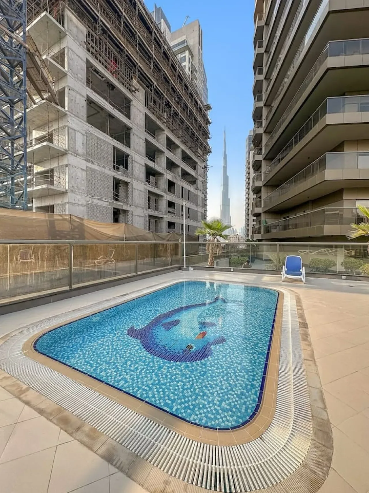 An outdoor swimming pool sits between two multi-story buildings under a clear sky.
