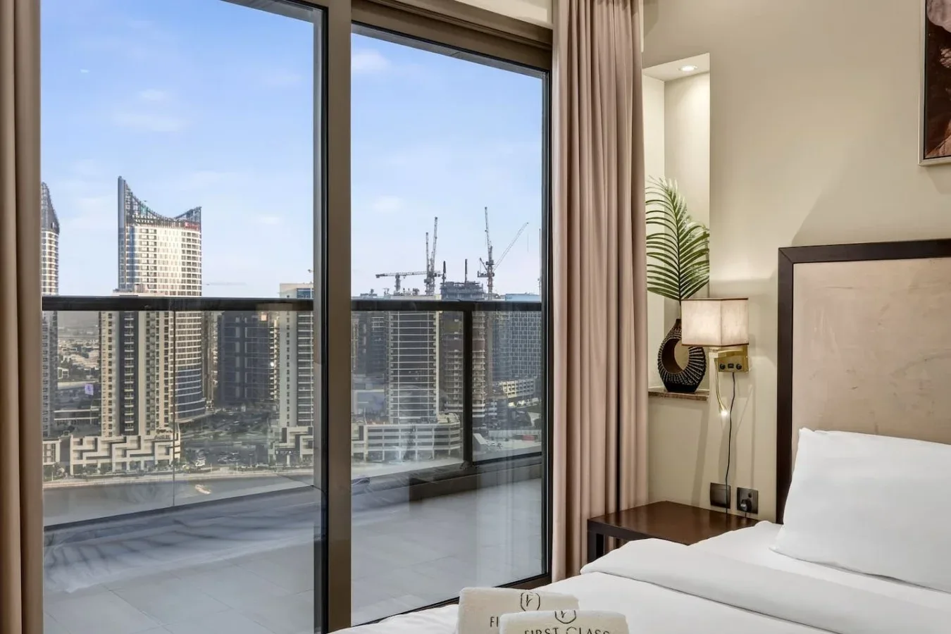 Un dormitorio con una cama junto a grandes ventanas con vistas a edificios de la ciudad.