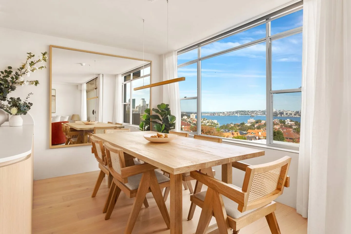 A bright dining area with a wooden table beside large windows overlooking the water.