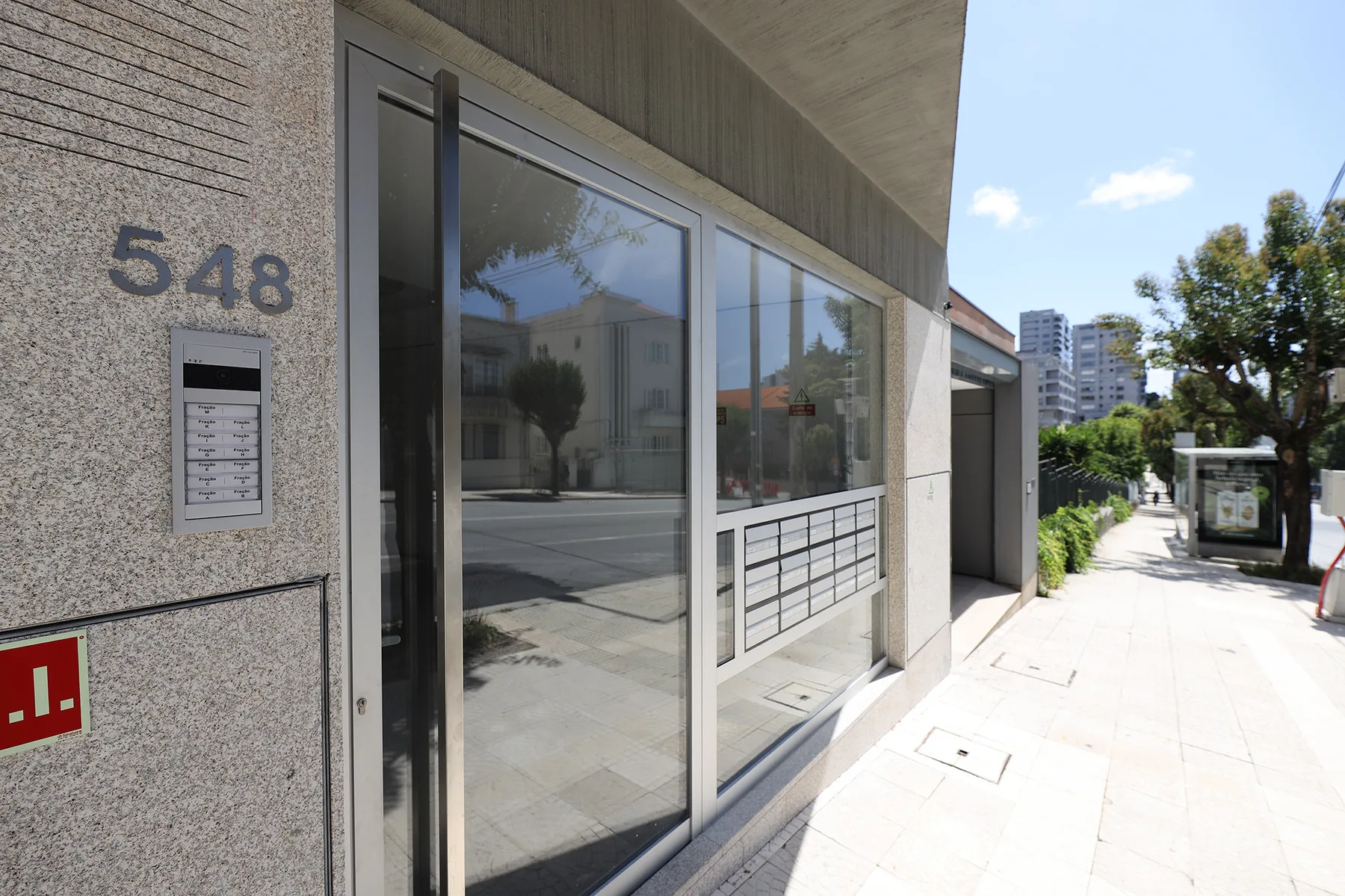 A glass-fronted building entrance opens onto a sunny sidewalk.