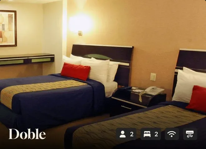 Two double beds with navy bedding and red pillows in a beige hotel room.