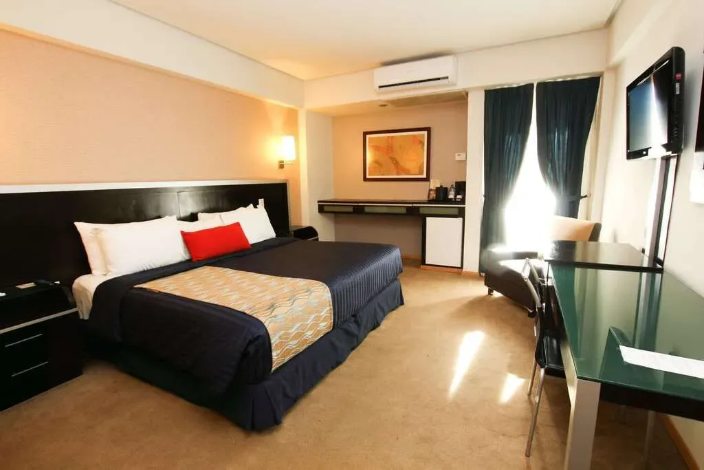 Modern hotel room with two beds, warm lighting, and a desk by the window.