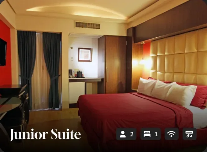 Junior suite with a red bed, padded headboard, dark curtains, and warm ambient lighting.