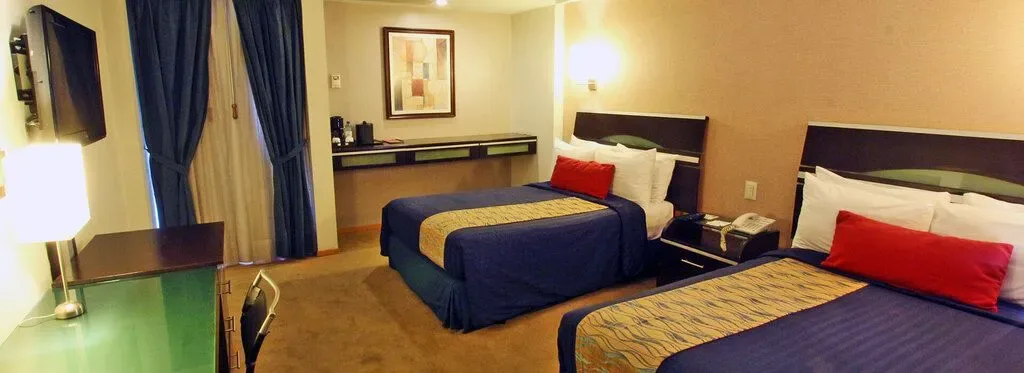 Hotel room with two beds, blue and red bedding, curtains, a lamp, and a television.