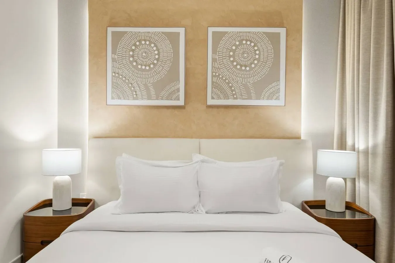Un dormitorio con una cama bien tendida bajo dos cuadros enmarcados.