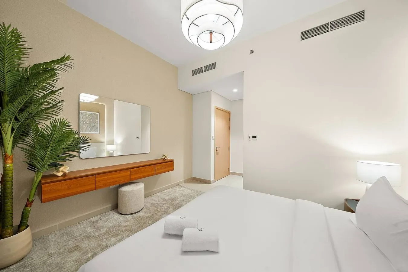 Un dormitorio luminoso con una cama, un tocador de pared y una planta en maceta.