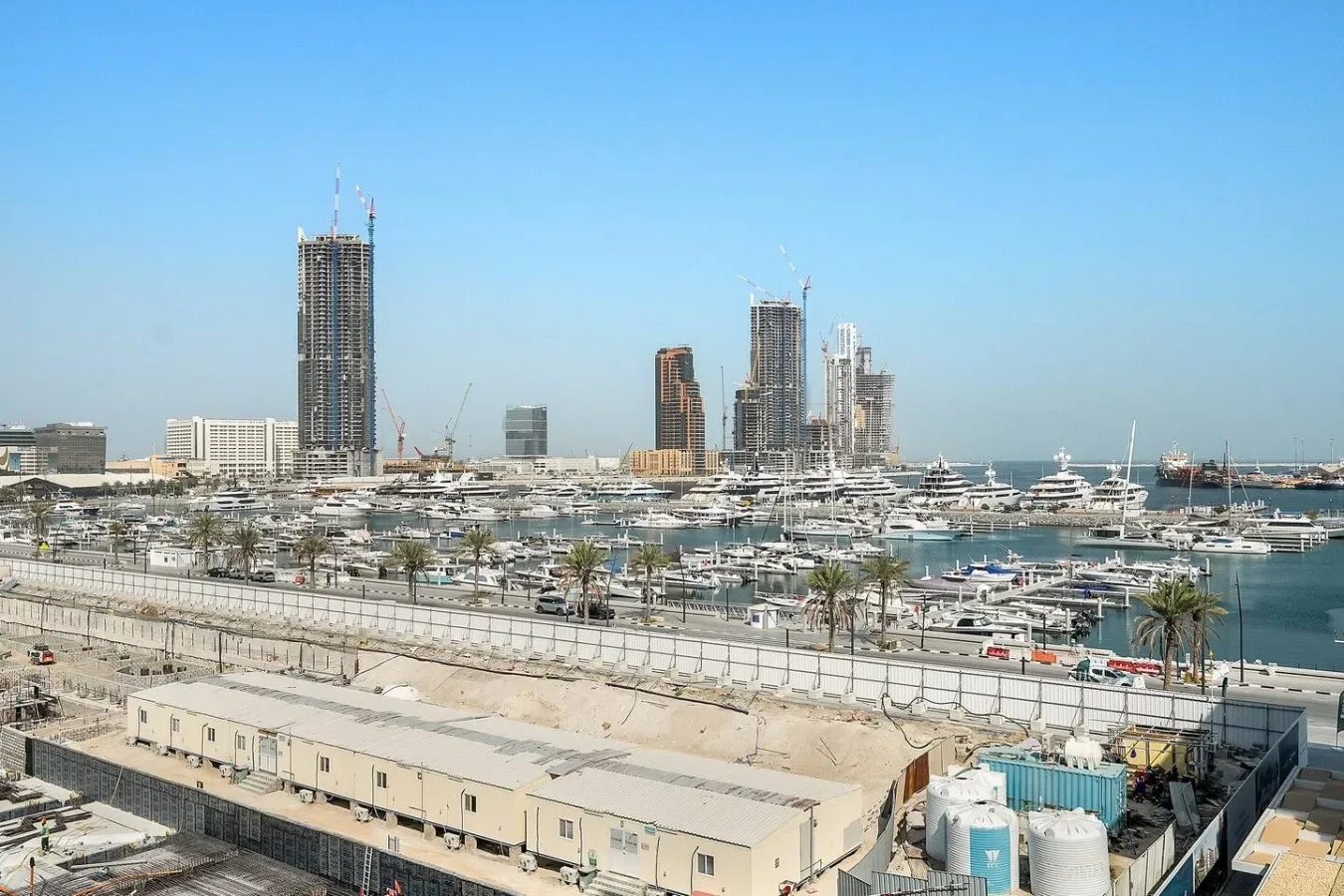 A marina filled with boats sits in front of a city skyline under construction.