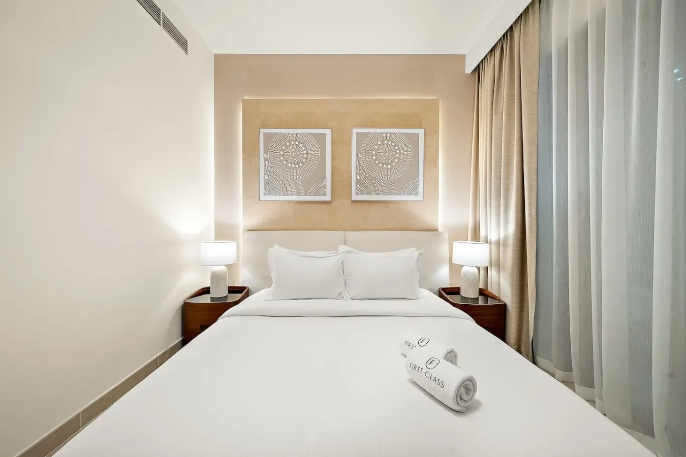 A bedroom with a neatly made bed, bedside tables, and framed wall art.