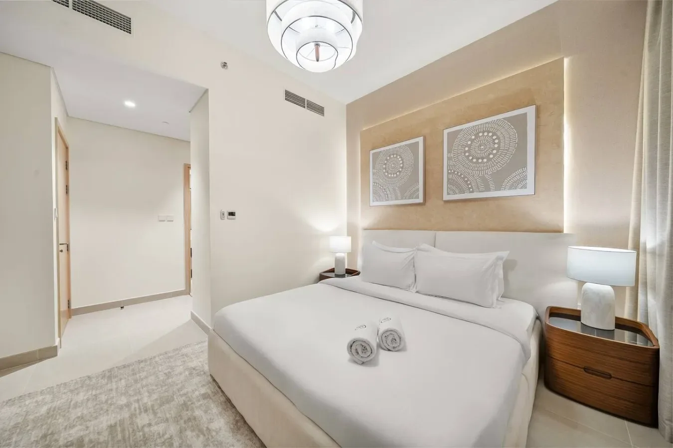 Un dormitorio luminoso con una cama bien tendida y cuadros sobre el cabecero.