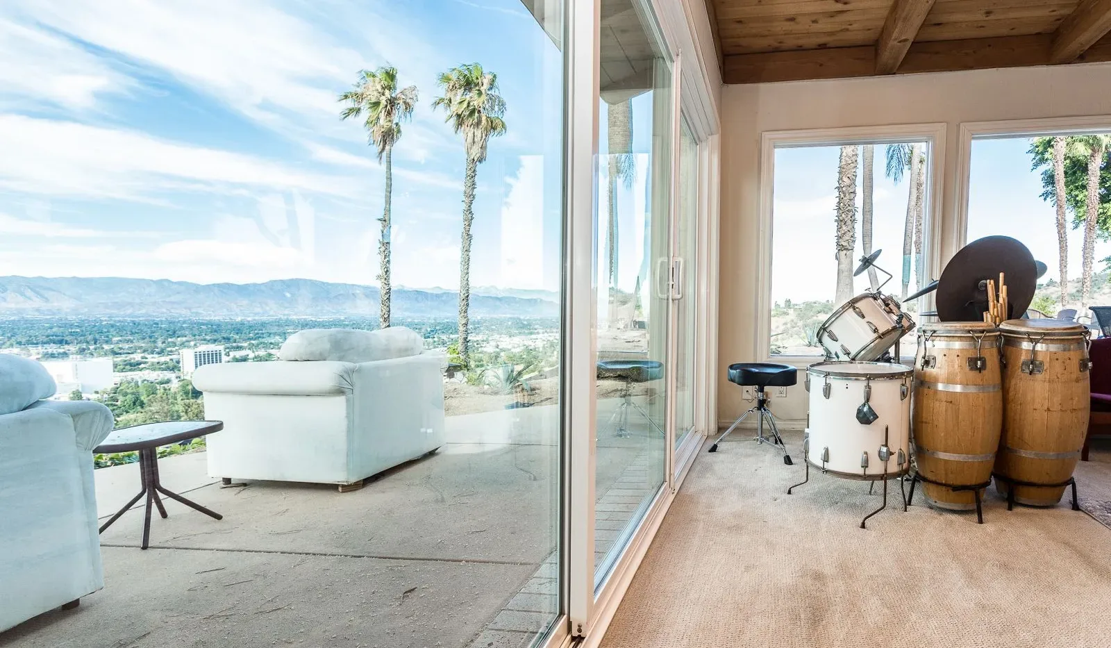 A bright living area opens onto a patio, with a drum set beside the windows.