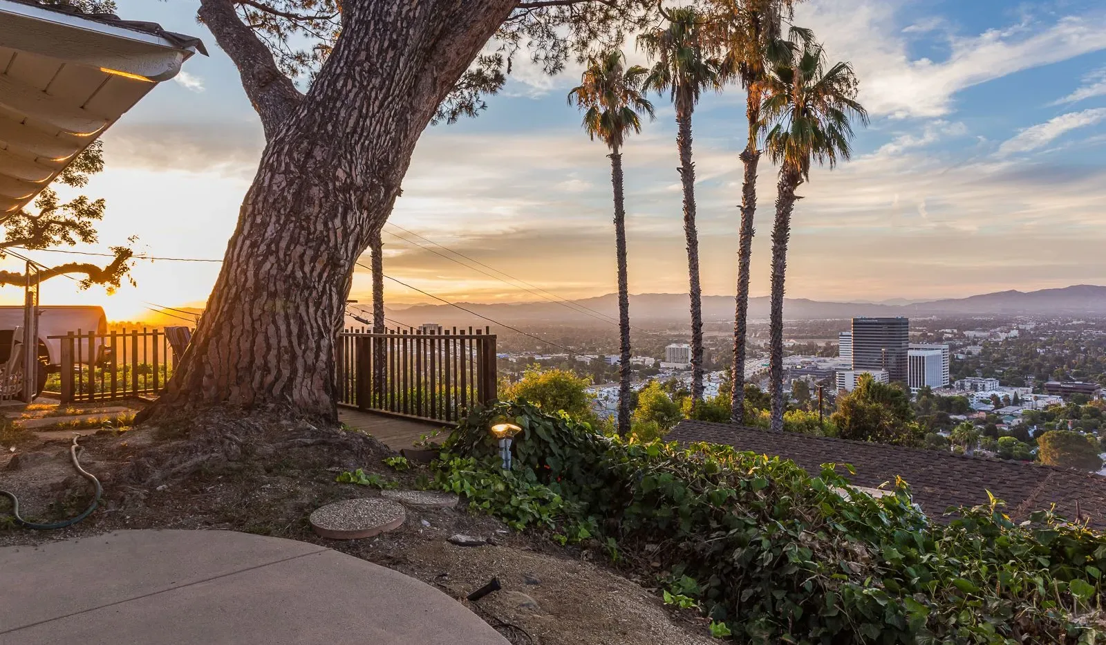 Un patio en una ladera ofrece vistas de la ciudad y colinas lejanas al atardecer.