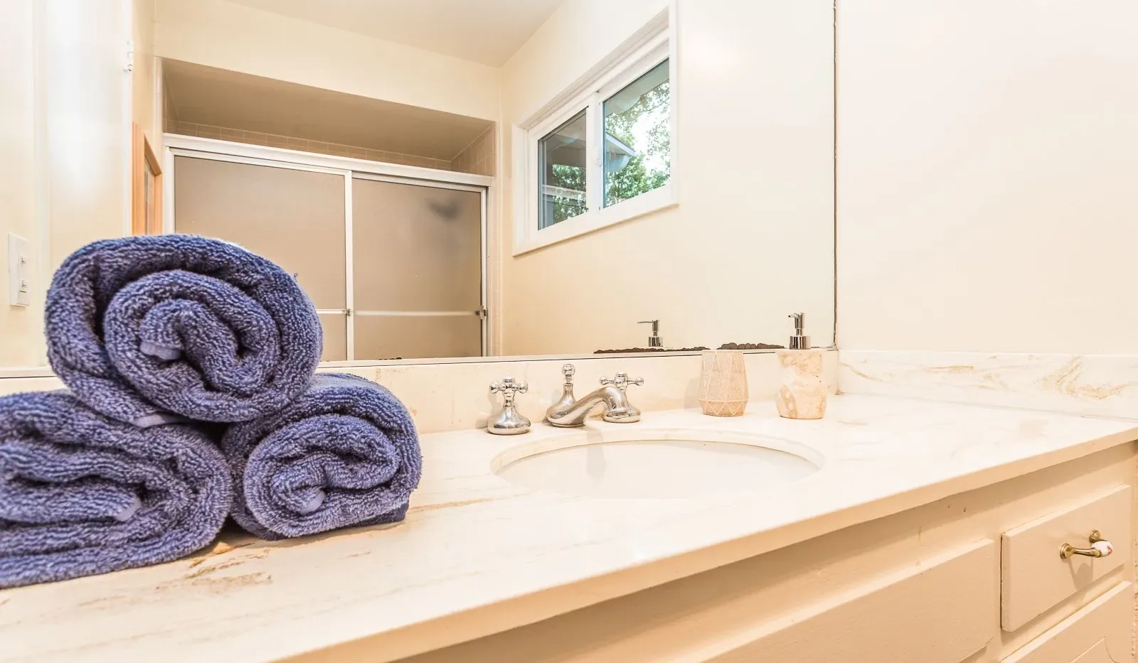 Un tocador de baño con toallas enrolladas junto al lavabo.
