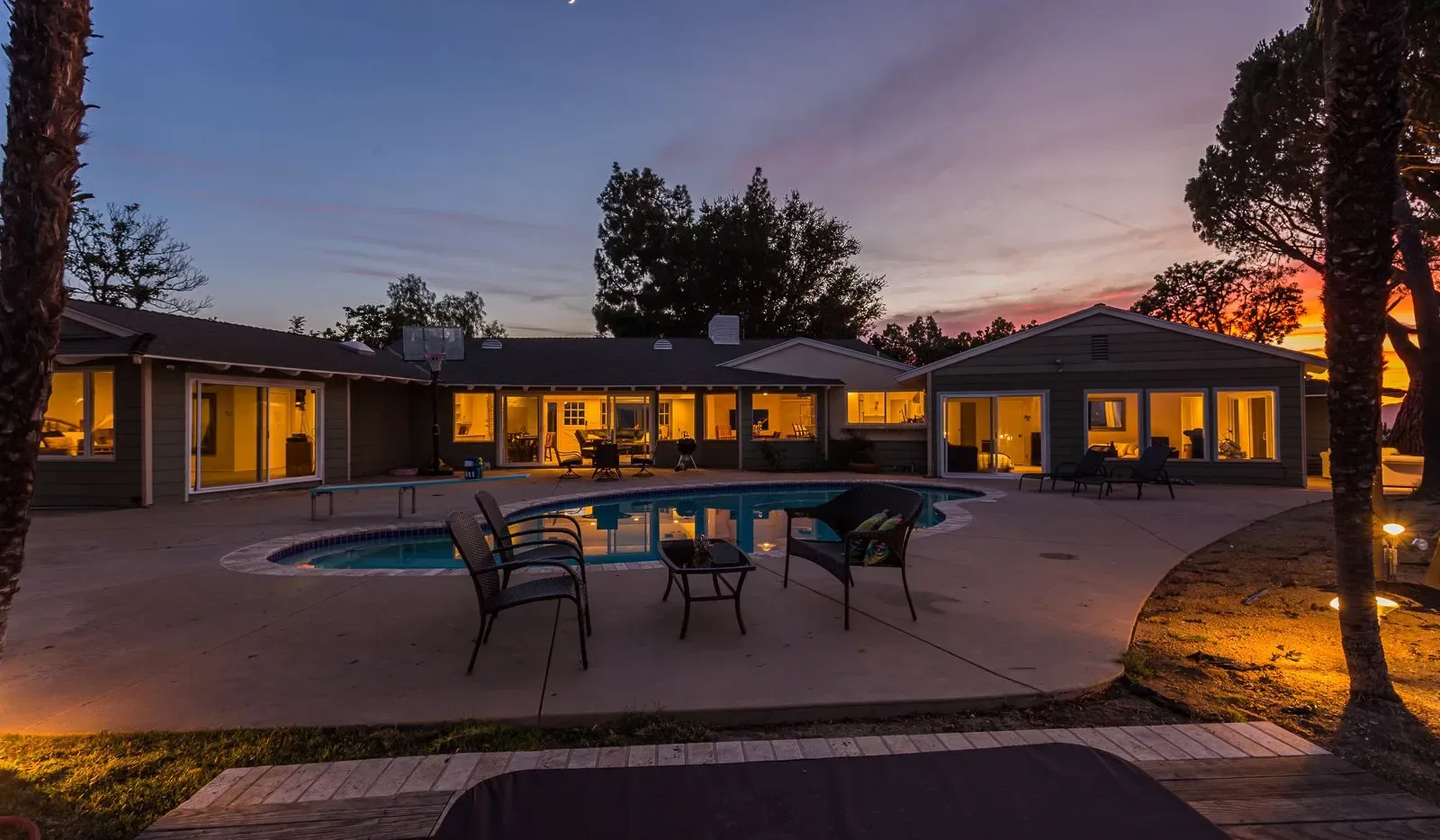 Una piscina exterior y un patio junto a una casa al atardecer.