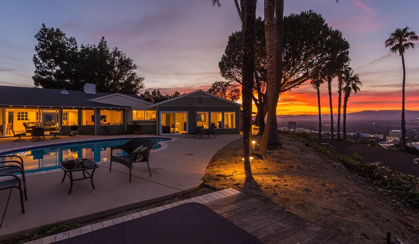 Una piscina y un patio junto a una casa baja miran hacia un atardecer colorido.